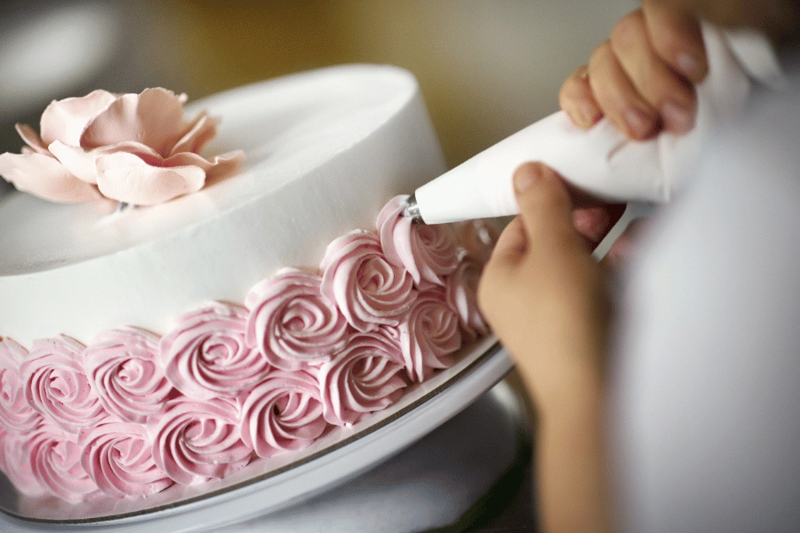 baker decorating a cake with pink frosting 